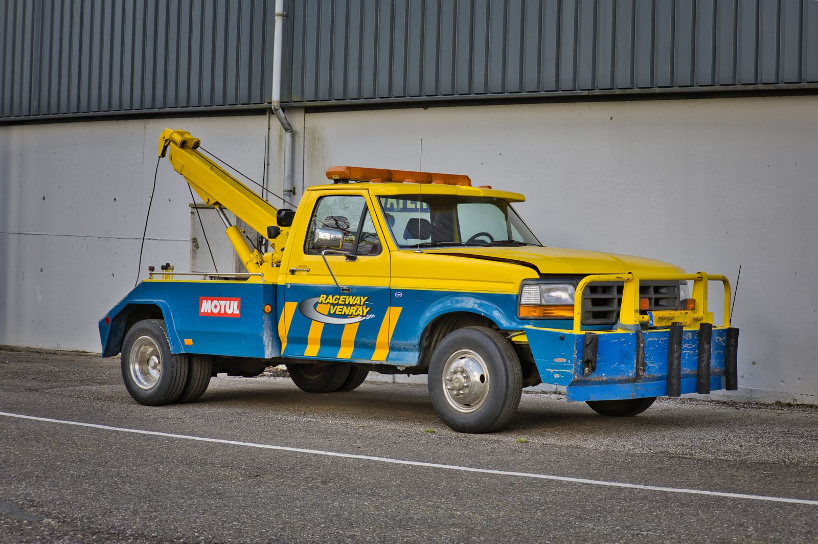 Yellow tow truck with its boom and hook stowed, parked ready for a call