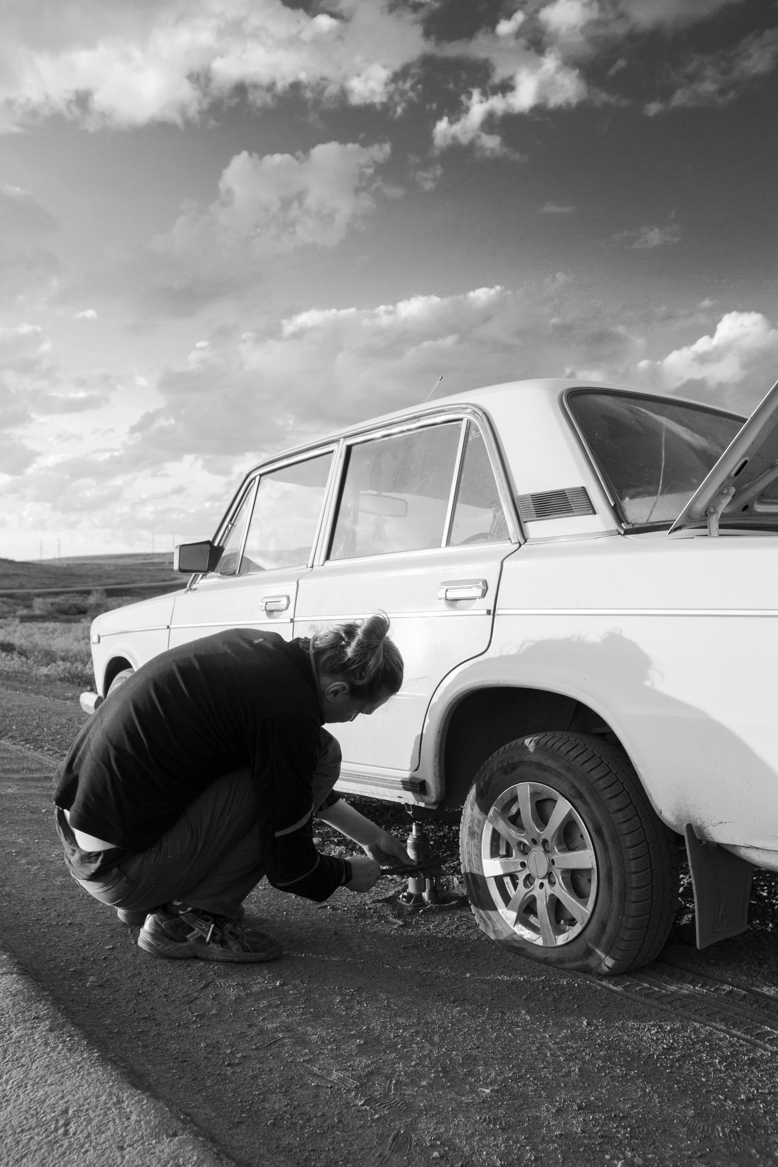 Roadside tire change in progress with the wheel off and the car up on a jack