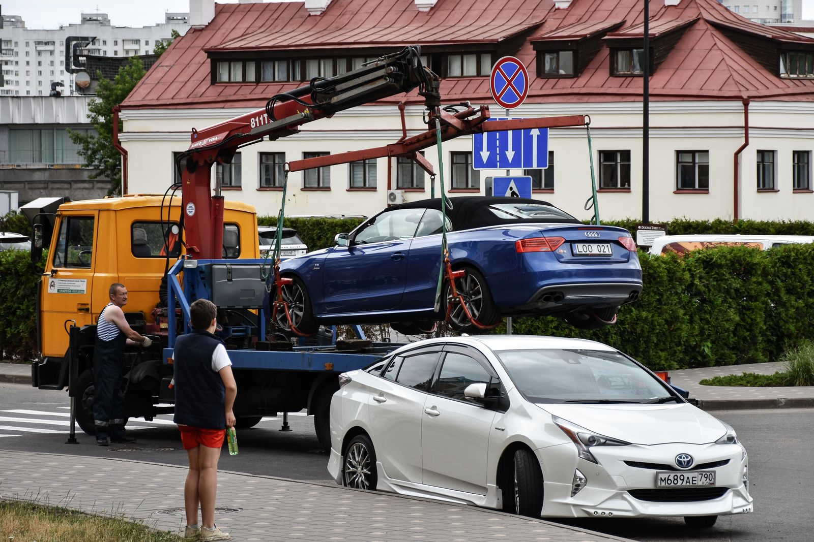 Low-clearance blue convertible winched onto the deck of a flatbed tow truck on a city street