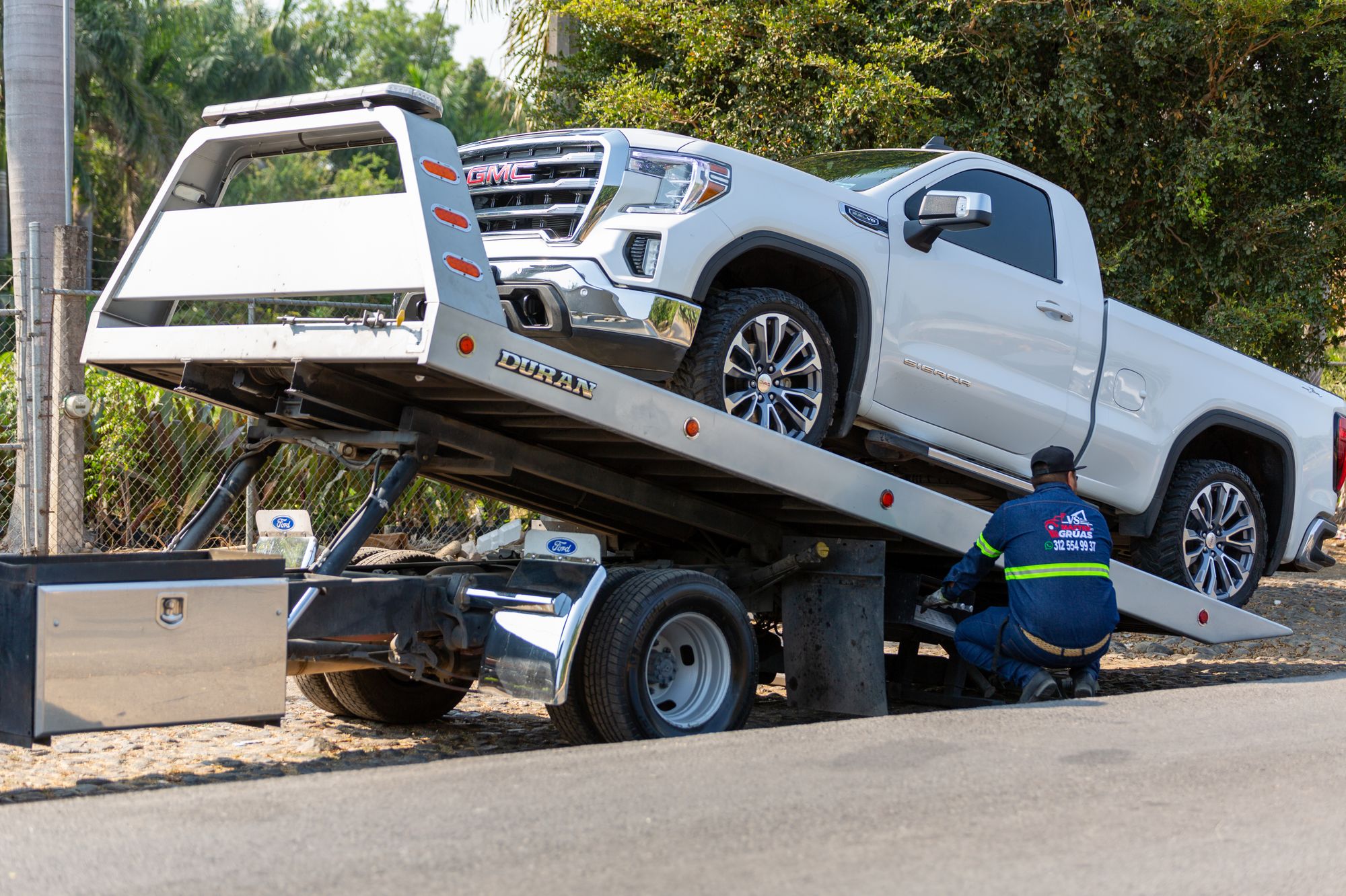 Tow truck operator winching a pickup onto a flatbed deck at the roadside in daylight