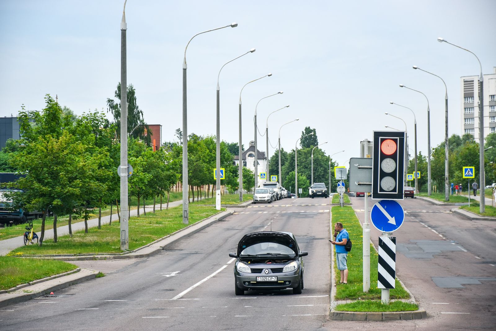 Driver standing beside a broken-down car at the edge of a road waiting for a tow truck