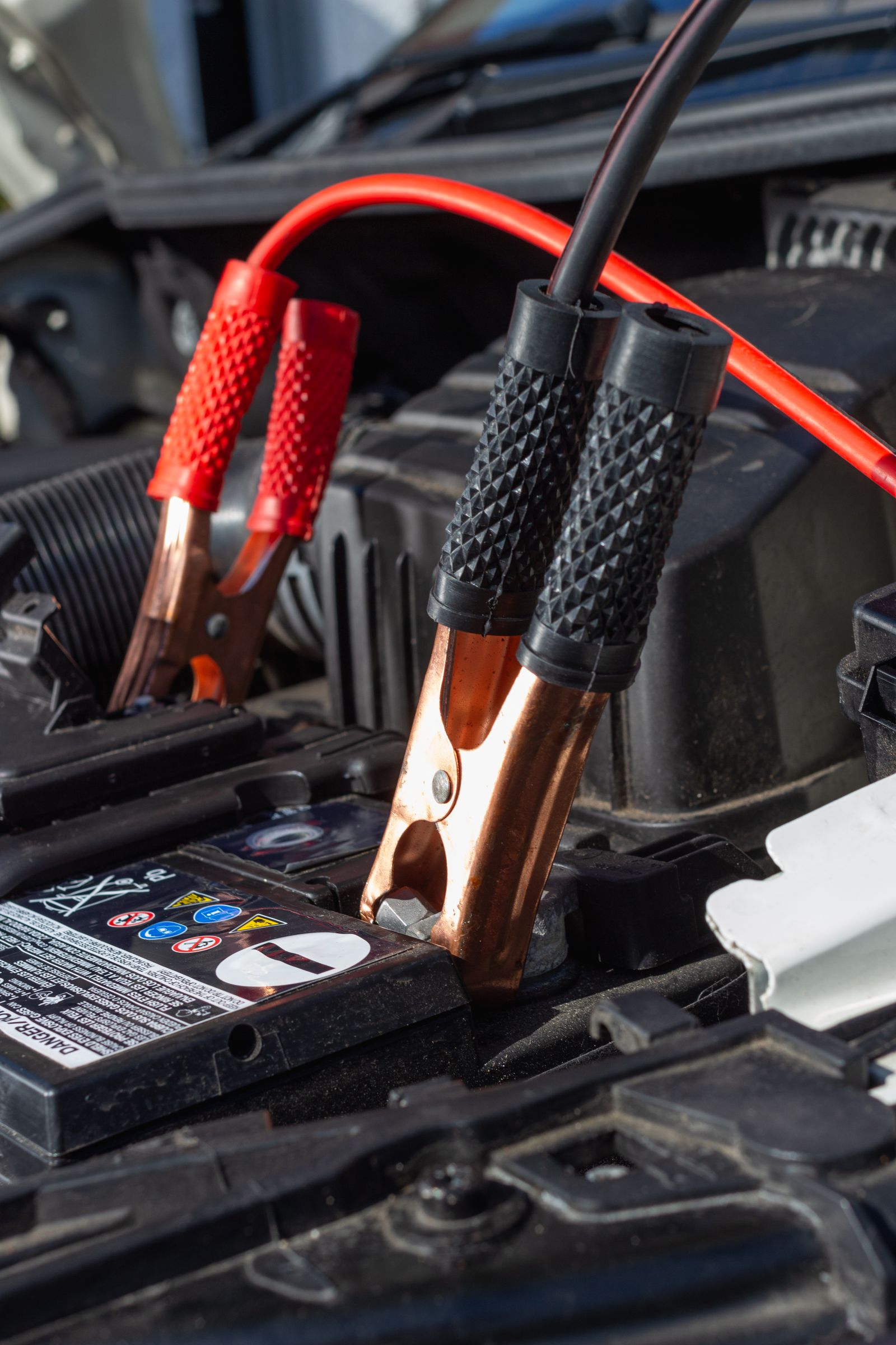 Red and black jumper cable clamps attached to a car battery terminal during a jump start