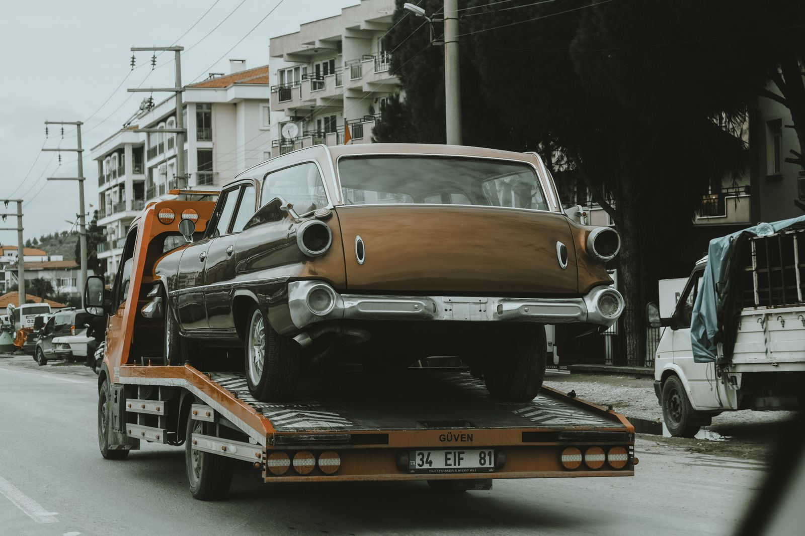 Car chained down on a tow truck deck setting off on a long distance tow out of town