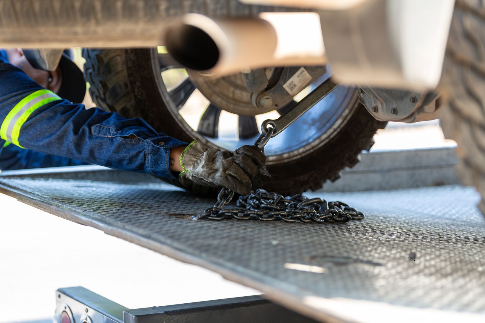 Operator ratcheting a securing chain onto a vehicle wheel strapped down on a tow truck deck