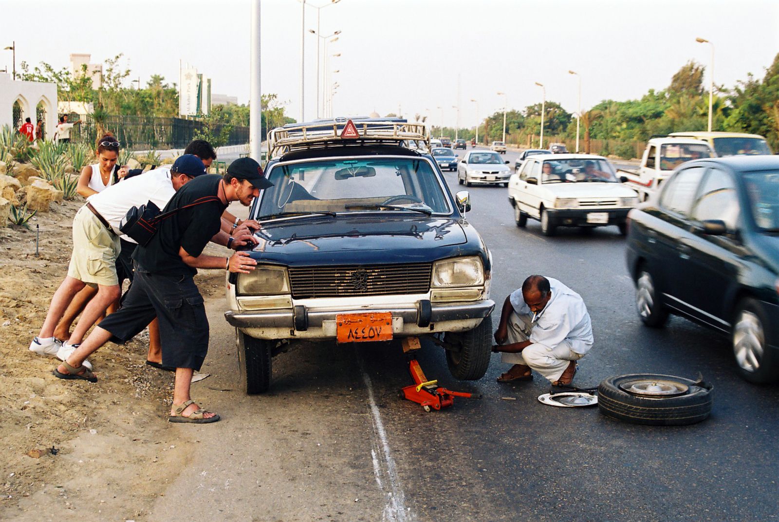 Car stopped at the edge of a busy road with the hood raised while a roadside repair is carried out
