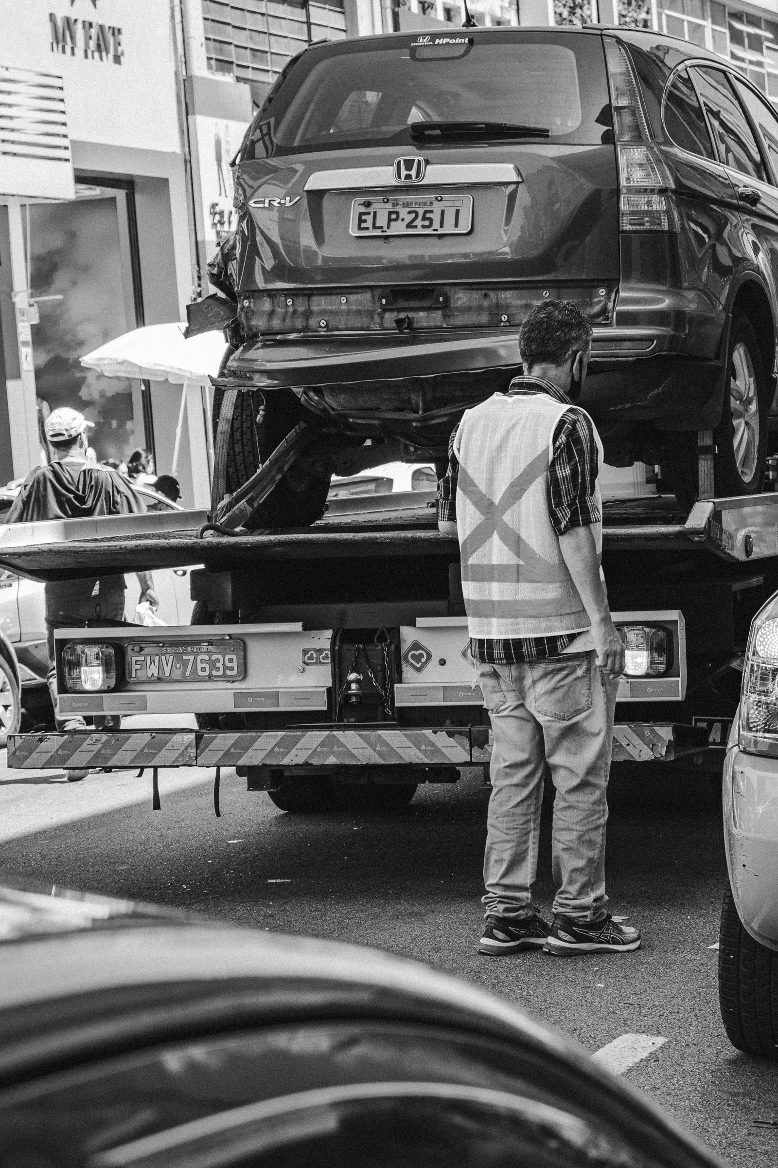 Tow truck winching a car up its tilted deck on a busy street while traffic passes