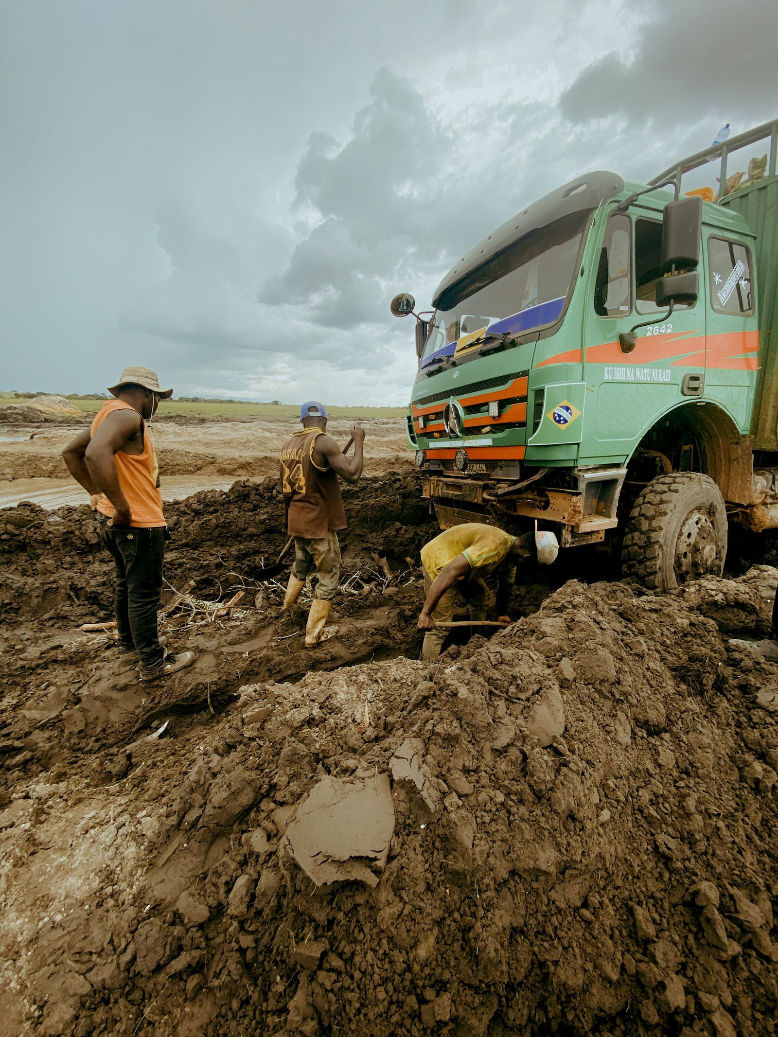 Recovery crew rigging a winch line to a truck buried to its axles in mud